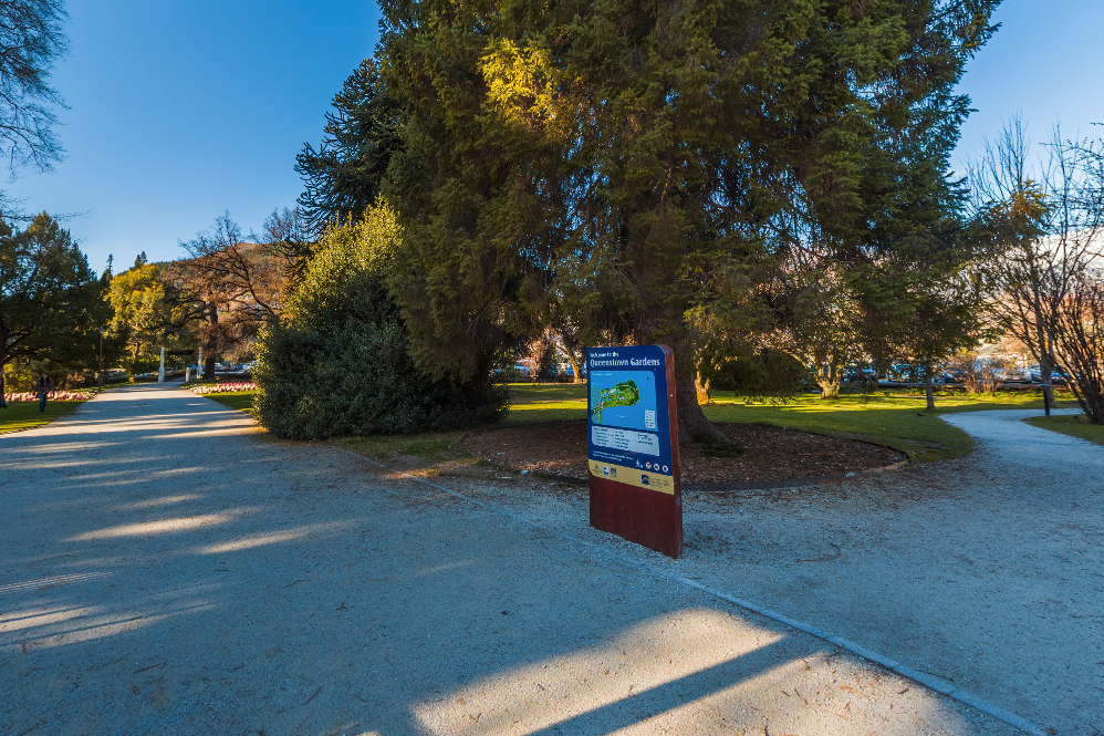 Wide gravel pathway with trees and a sign post with a map of gardens