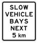 White road sign with black text that says slow vehicle bays next 5km
