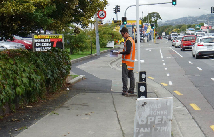 a person in high-visibility clothing is undertaking a safety audit on a footpath 