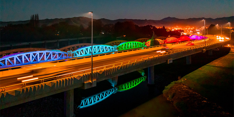 The old banana bridge at night with panels lit up in different colours along the bridge.